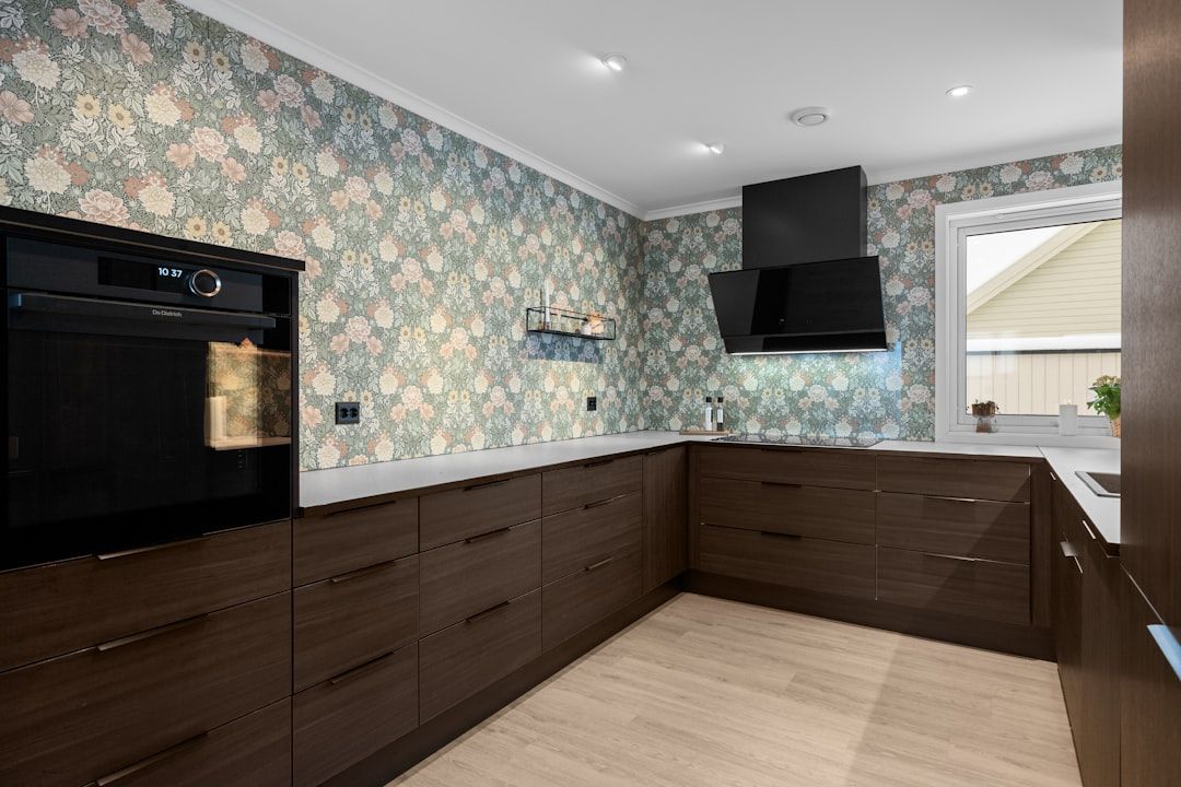 Kitchen with dark brown cabinets, floral wallpaper, and a built-in oven. A range hood and a window are also visible.