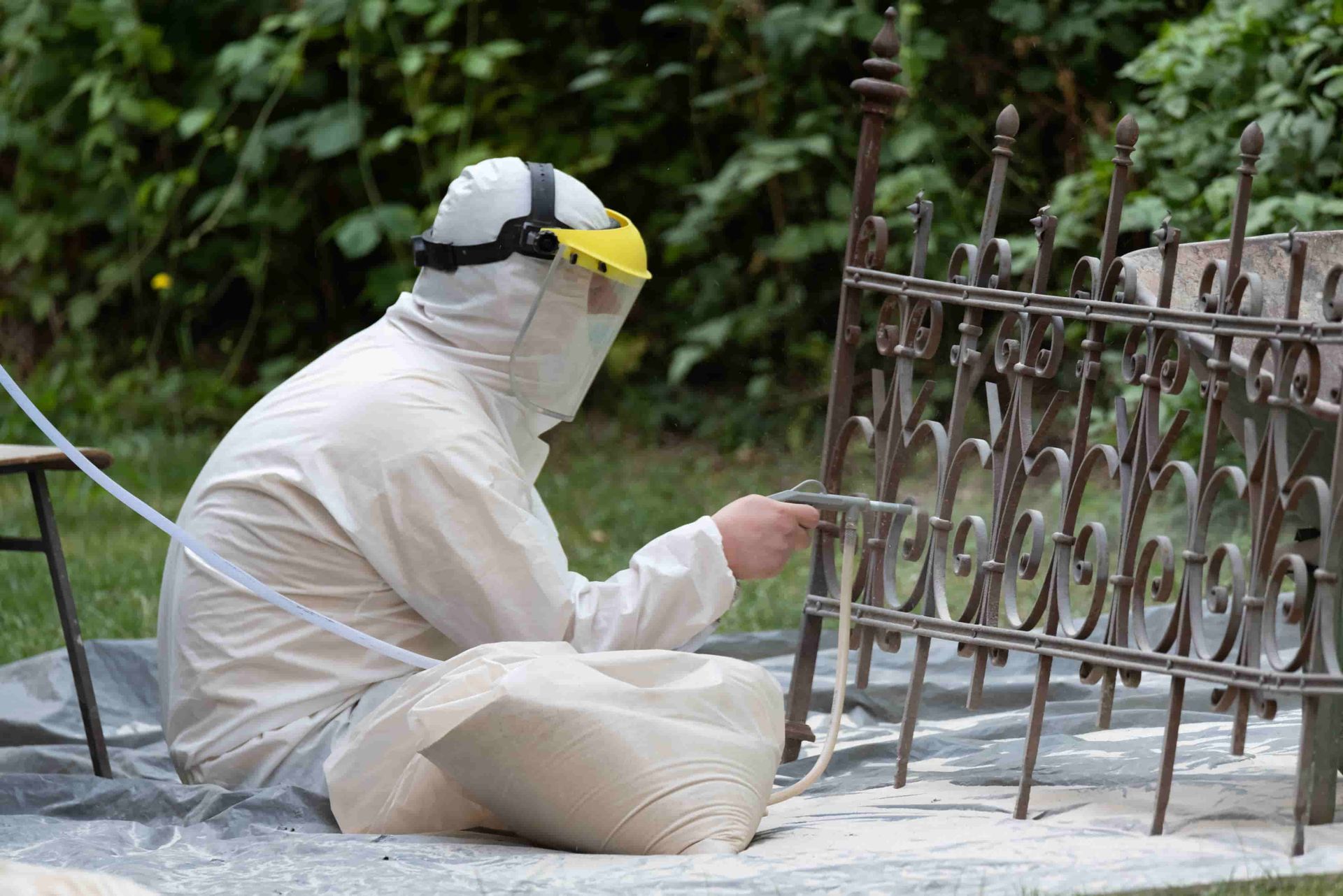 A man is sitting on the ground sand blasting a wrought iron fence — Mudgee Powder Coat Pty Ltd in Mudgee, NSW