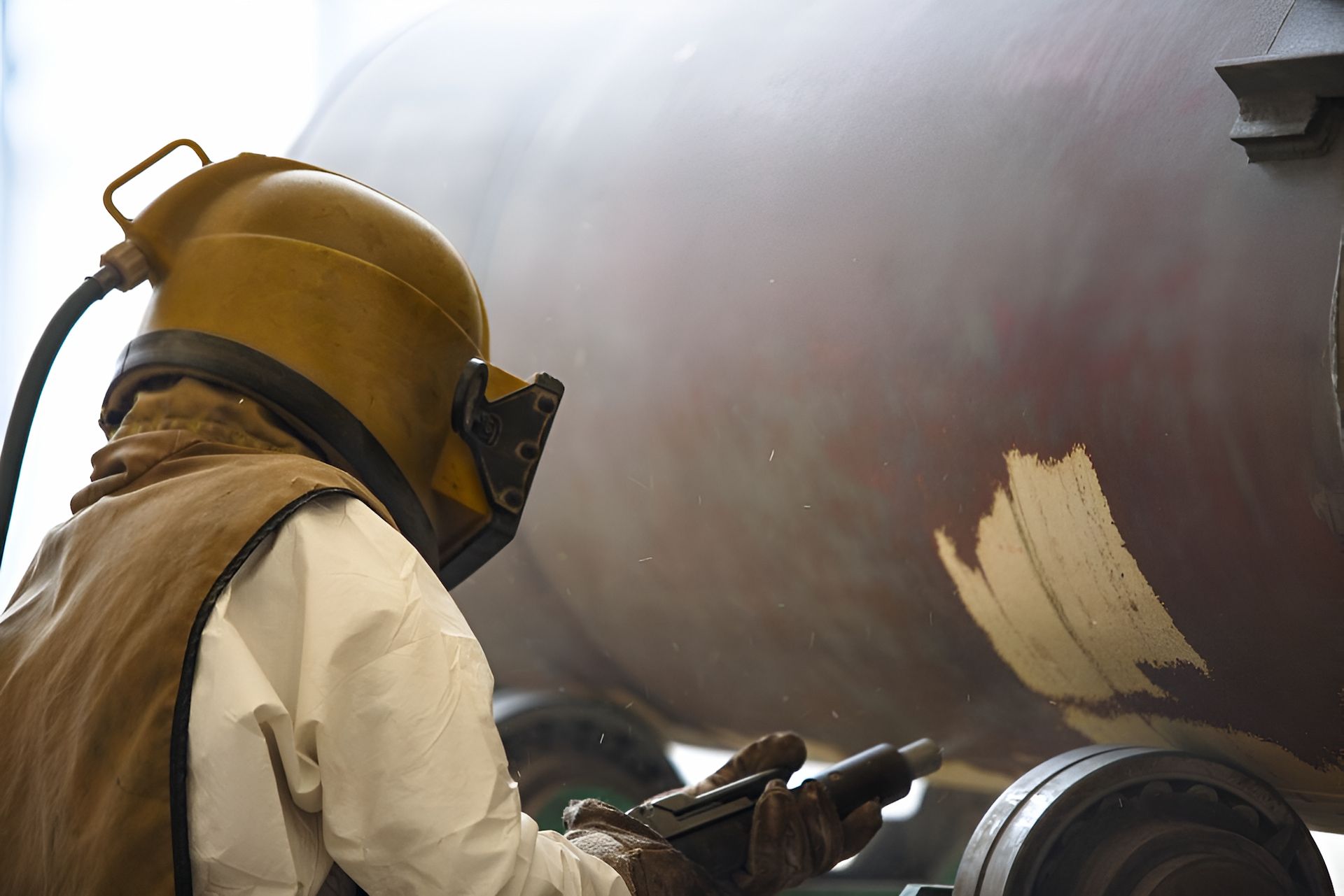 A Man Wearing a Helmet and Gloves is Sandblasting a Piece of Metal — Mudgee Powder Coat Pty Ltd in Kandos, NSW