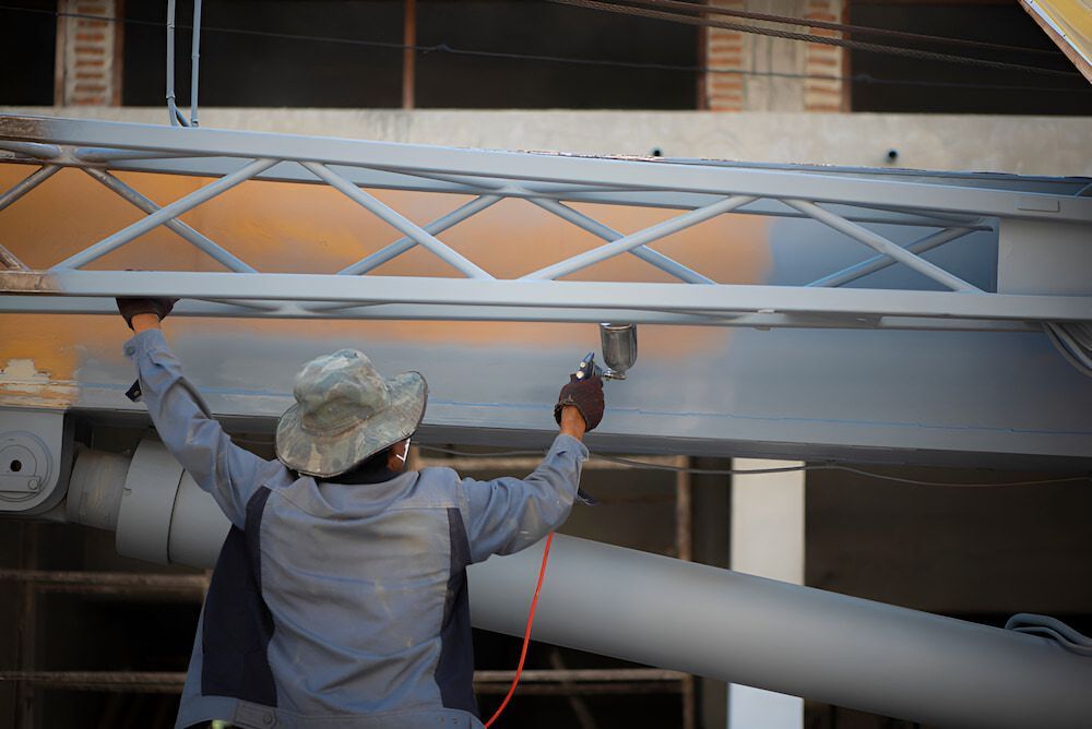 a Man is Painting a Metal Structure on a Construction Site — Mudgee Powder Coat Pty Ltd in Mudgee, NSW