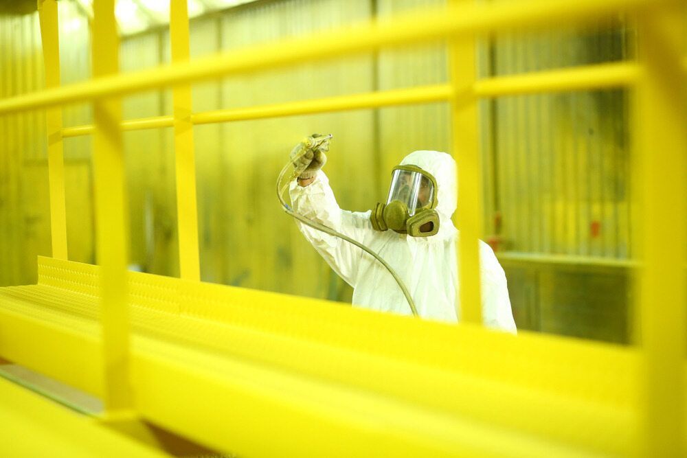 A Man Wearing a Gas Mask is Spray Painting a Yellow Railing — Mudgee Powder Coat Pty Ltd in Mudgee, NSW