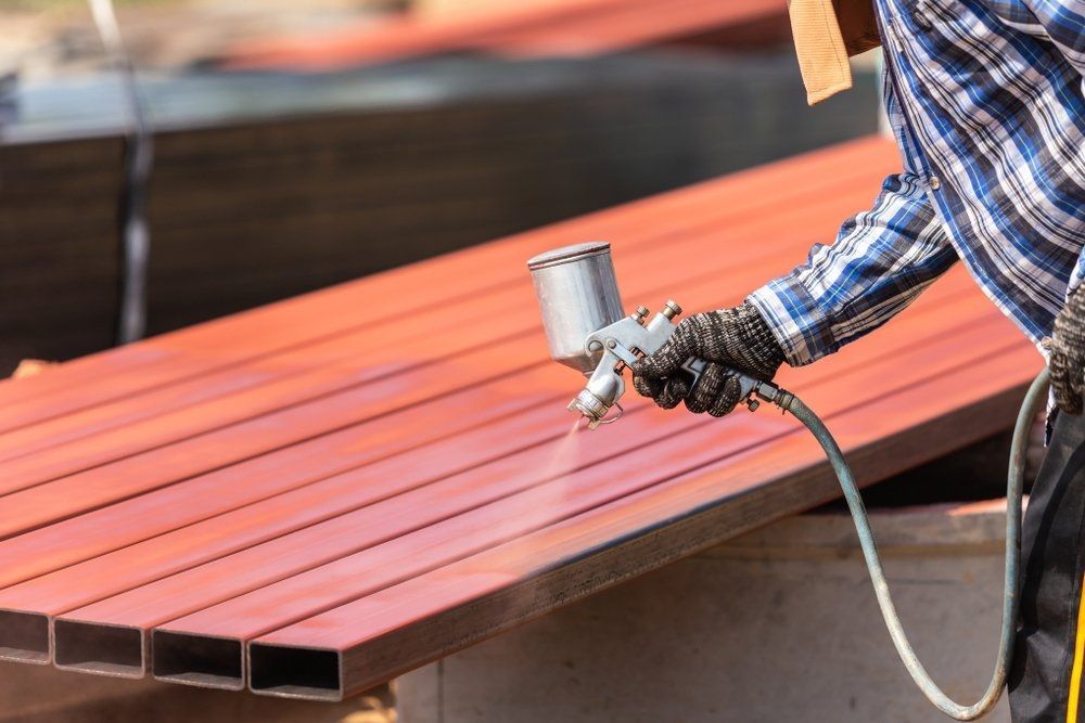 Worker in a White Suit and Mask Using a Spray Gun to Apply Paint — Mudgee Powder Coat Pty Ltd in Mudgee, NSW