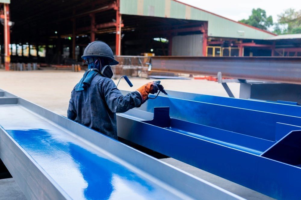 A Man is Spray Painting a Blue Metal Structure in a Factory — Mudgee Powder Coat Pty Ltd in Mudgee, NSW