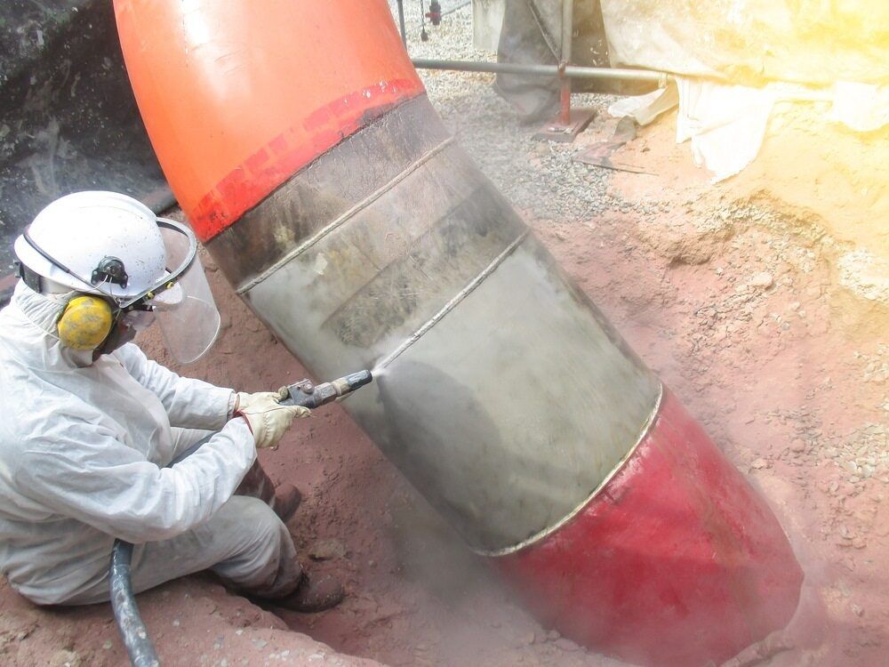 A Man in a Protective Suit is Cleaning a Large Pipe in the Dirt — Mudgee Powder Coat Pty Ltd in Rylstone, NSW