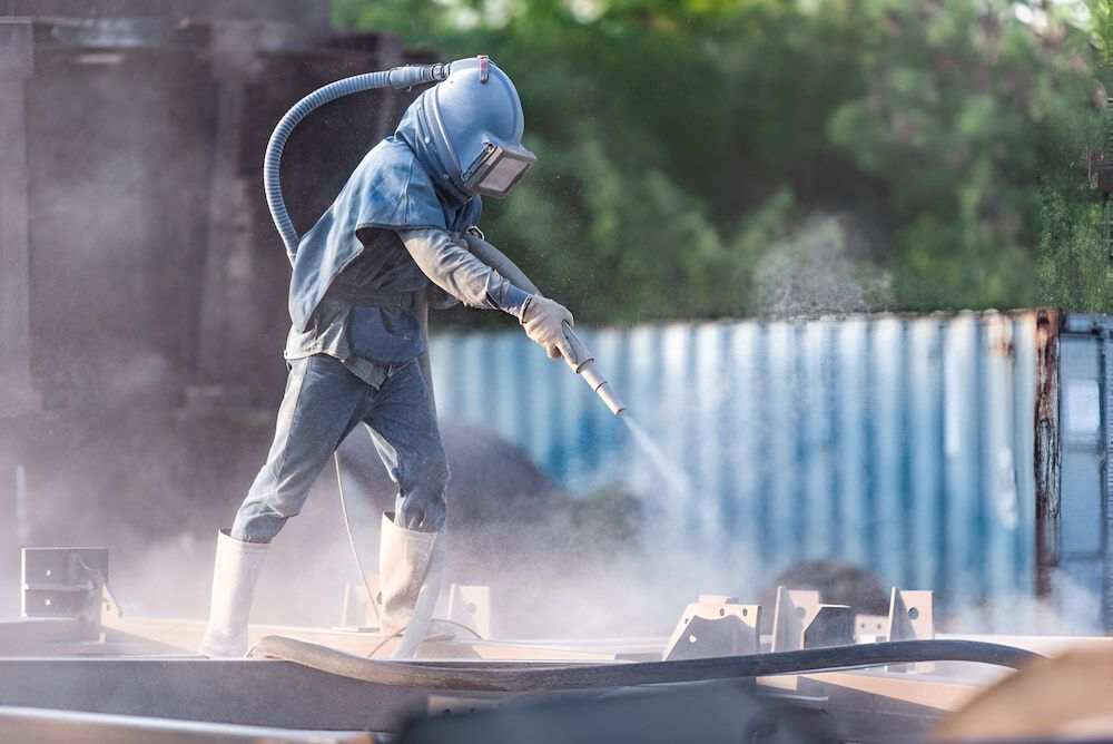 A Man in a Protective Suit is Sandblasting a Piece of Metal — Mudgee Powder Coat Pty Ltd in Mudgee, NSW