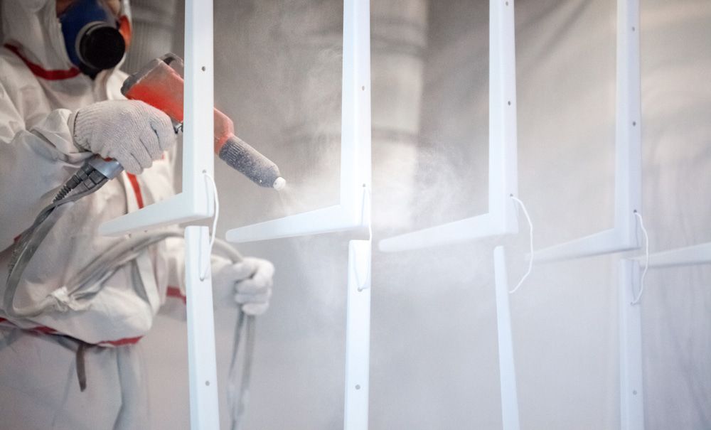 A Man in a Protective Suit is Spray Painting a Metal Structure — Mudgee Powder Coat Pty Ltd in Mudgee, NSW