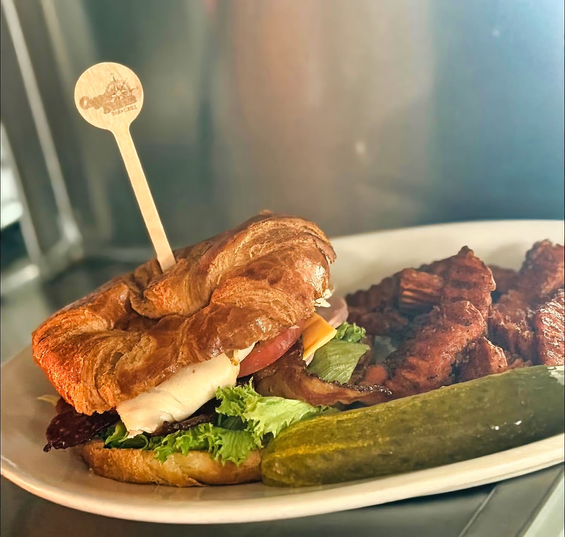 Croissant sandwich served with steak fries and pickle.