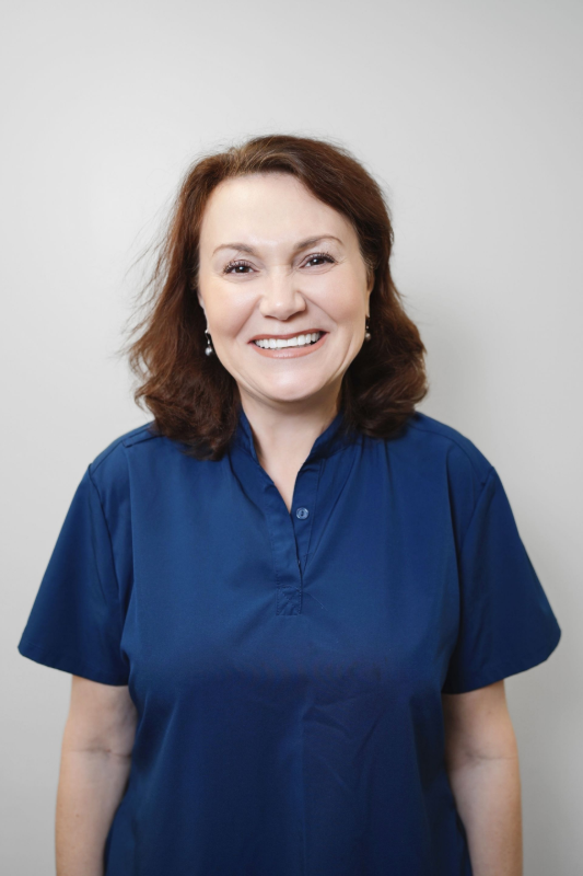 Woman with red-brown hair wearing blue scrubs, smiling.