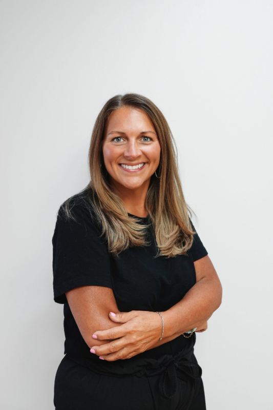 Woman with crossed arms smiling, wearing black, in front of a white backdrop.