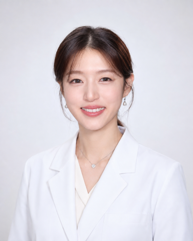 Smiling person in a white blazer against a light gray background.