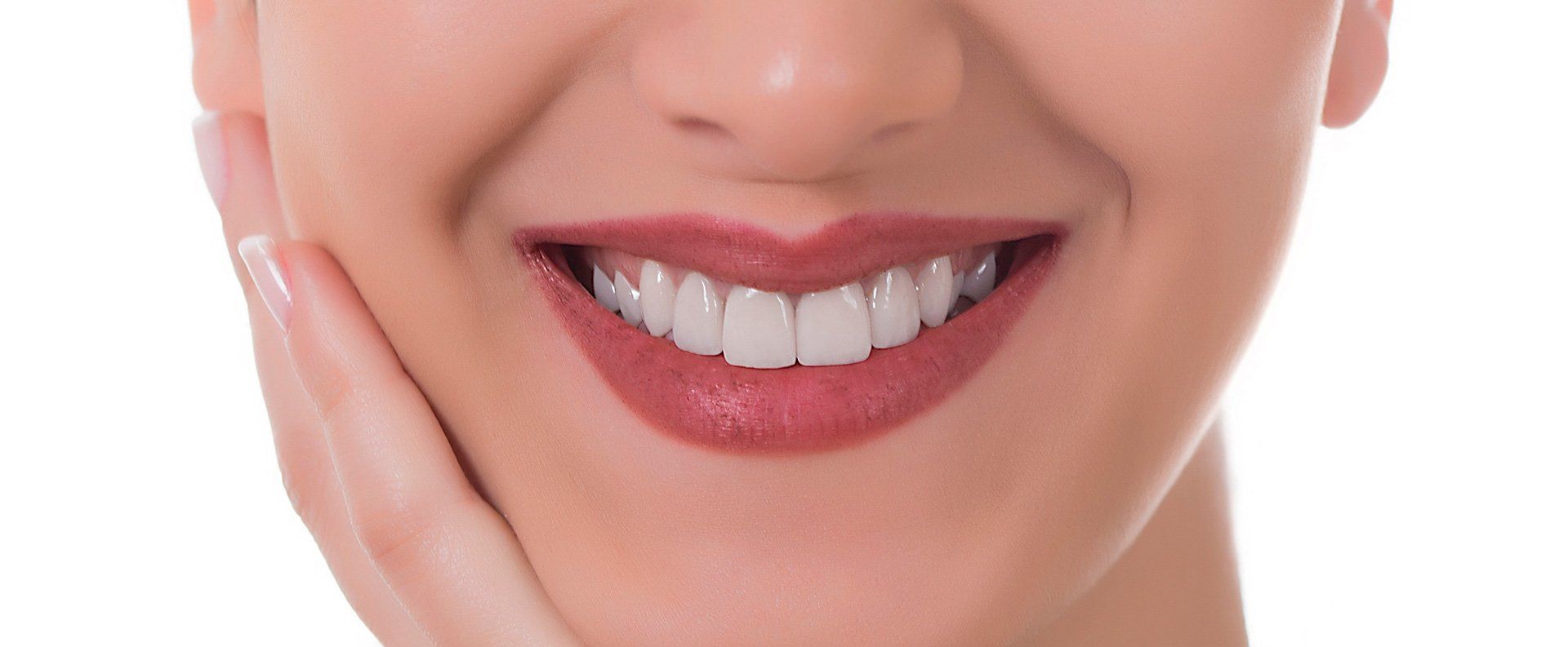 Close-up of a woman smiling, showing white teeth and wearing red lipstick. She is holding her hand up to her face.