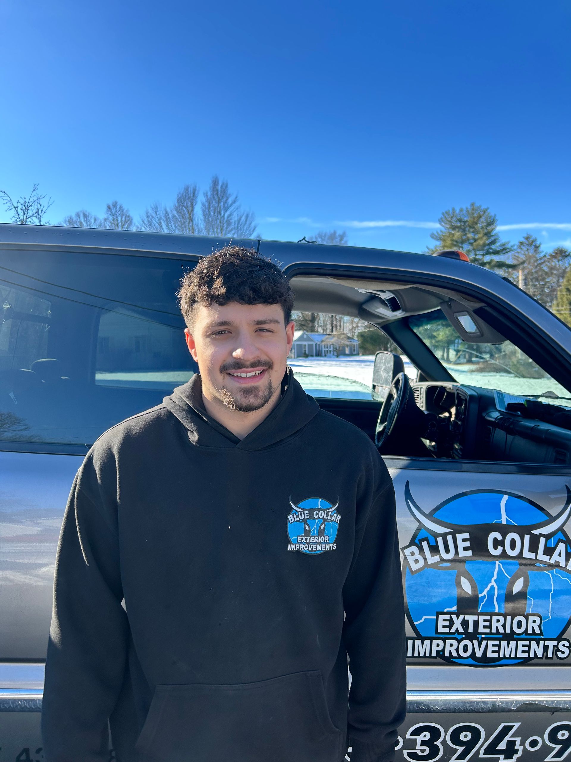 Man in a black hoodie stands beside a truck, logo for