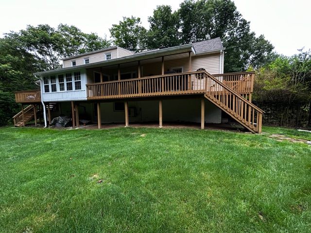 Two-story house with large wooden deck, stairs, and covered porch, set on a green lawn.