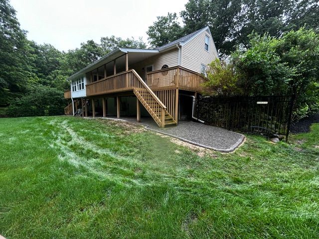 Wooden deck of a house, set on green lawn with a gravel driveway.