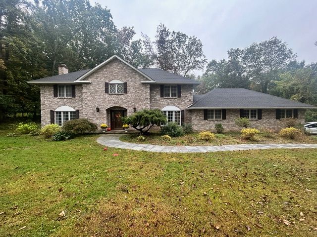 Two-story brick house with a dark roof and a curved walkway, surrounded by trees and grass.