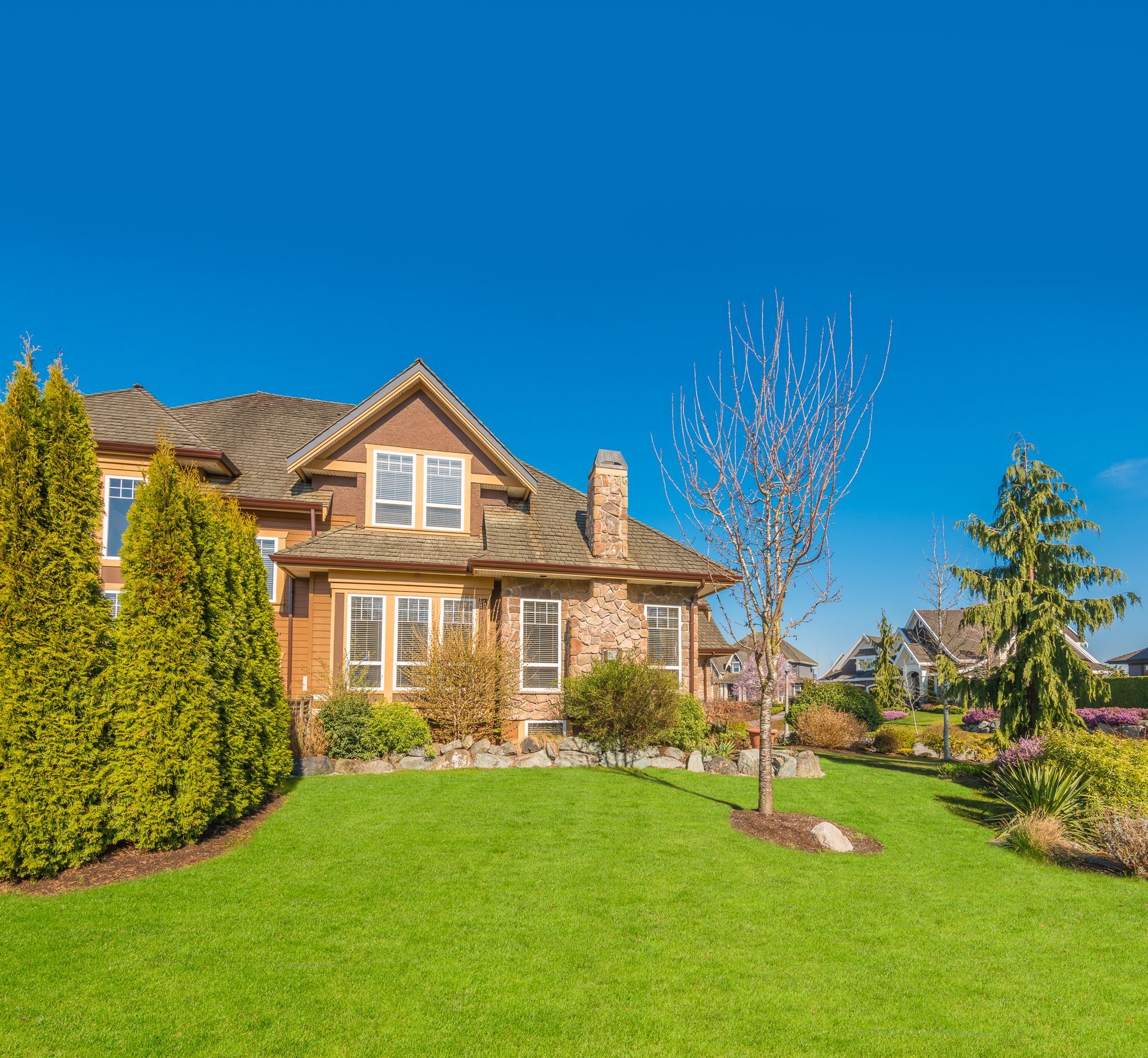 Suburban stone house with a manicured green lawn and clear blue sky