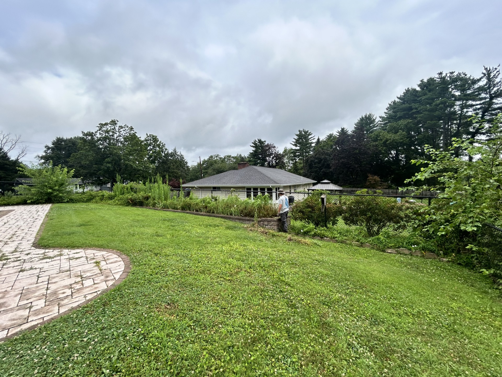 A small, white building with a dark roof surrounded by green grass and trees under an overcast sky.