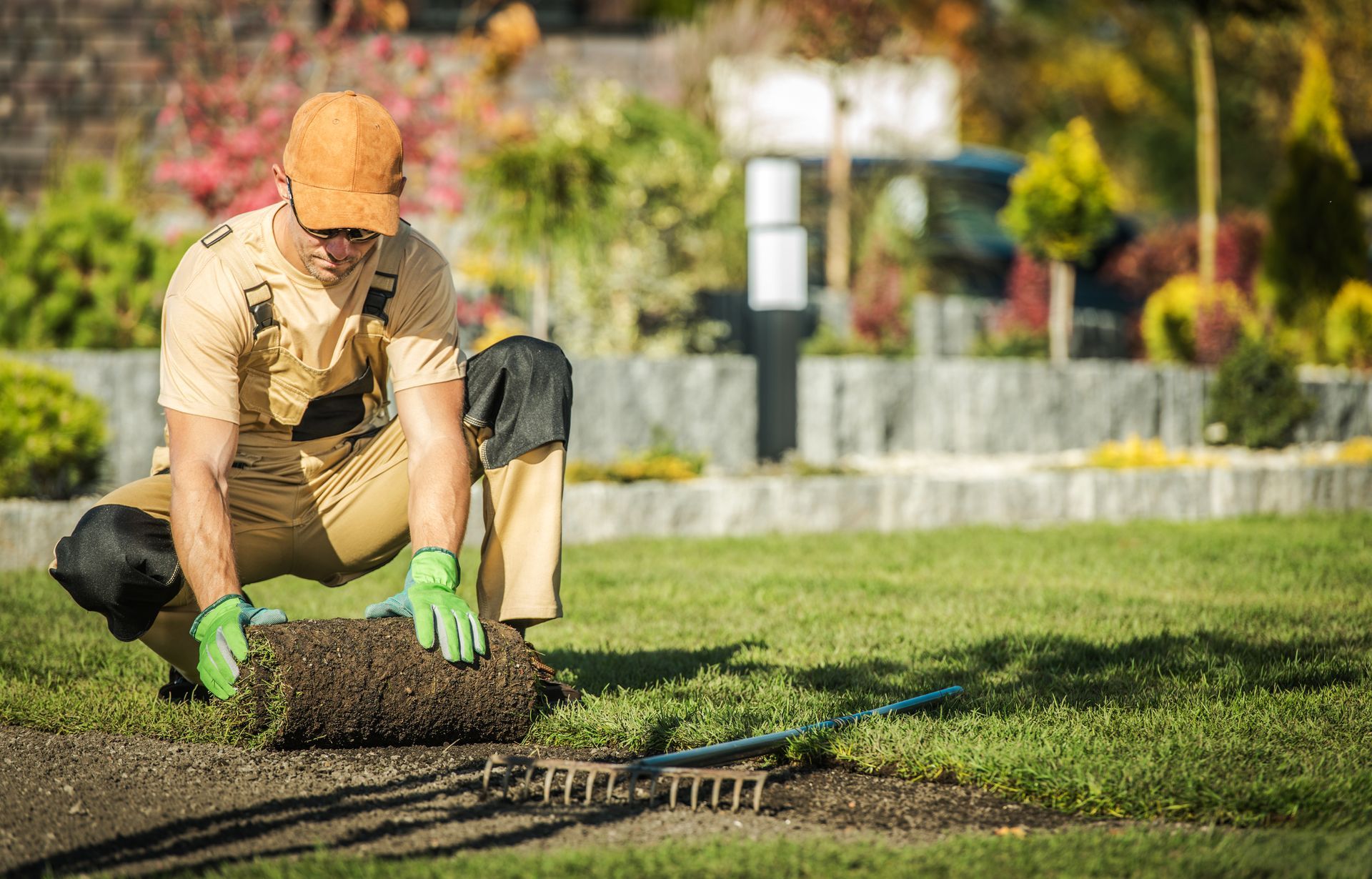 Gardener in tan clothes and green gloves lifting sod in a sunny landscaped yard