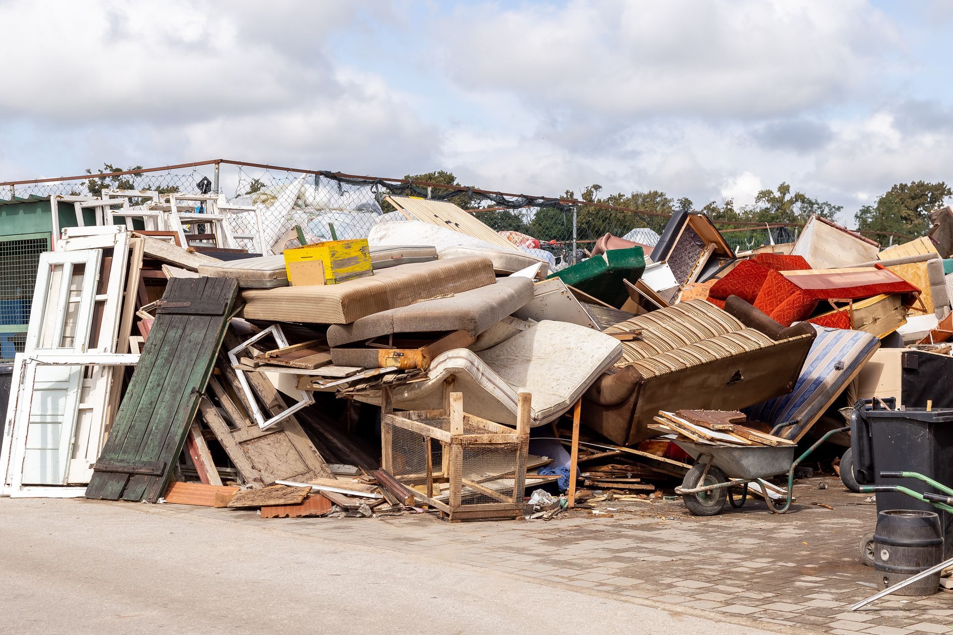 Pile of discarded furniture and construction debris at a dump, under a cloudy sky.