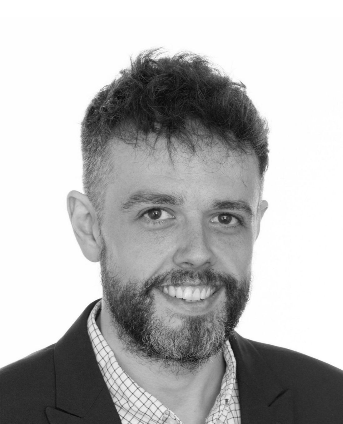 Man in blazer, smiling, short dark hair, short beard, light-colored shirt.