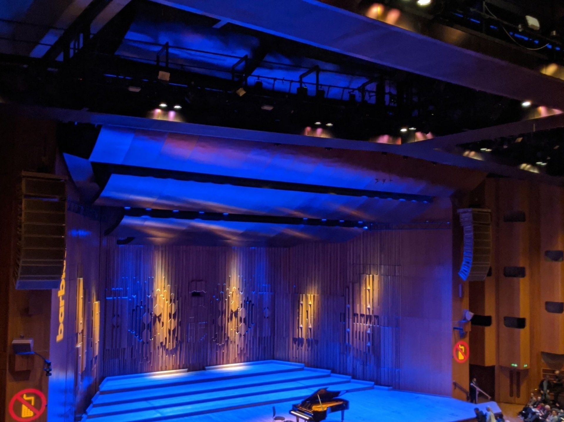 Stage with blue and yellow lighting, piano visible, wooden backdrop.