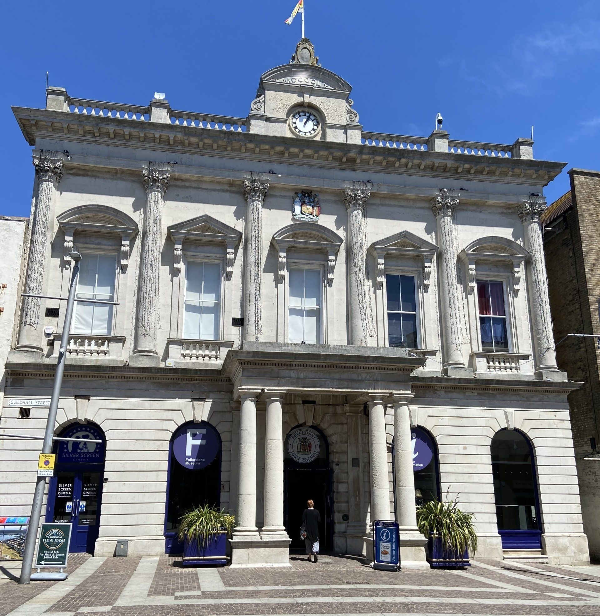 Elegant stone building with columns and a clock tower, featuring shop fronts below.
