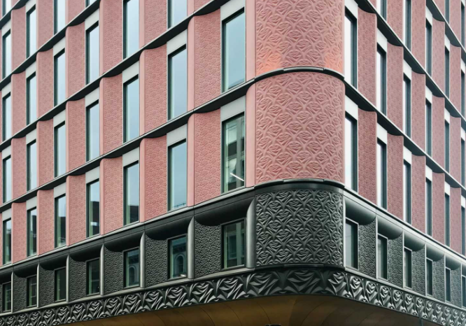 Corner view of a modern building with red brick and dark gray textured facade. Vertical windows, overcast sky.