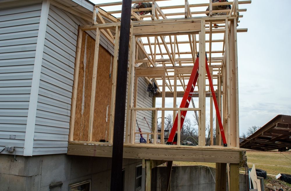 A partially constructed wooden room addition attached to the side of a house with a red ladder inside.