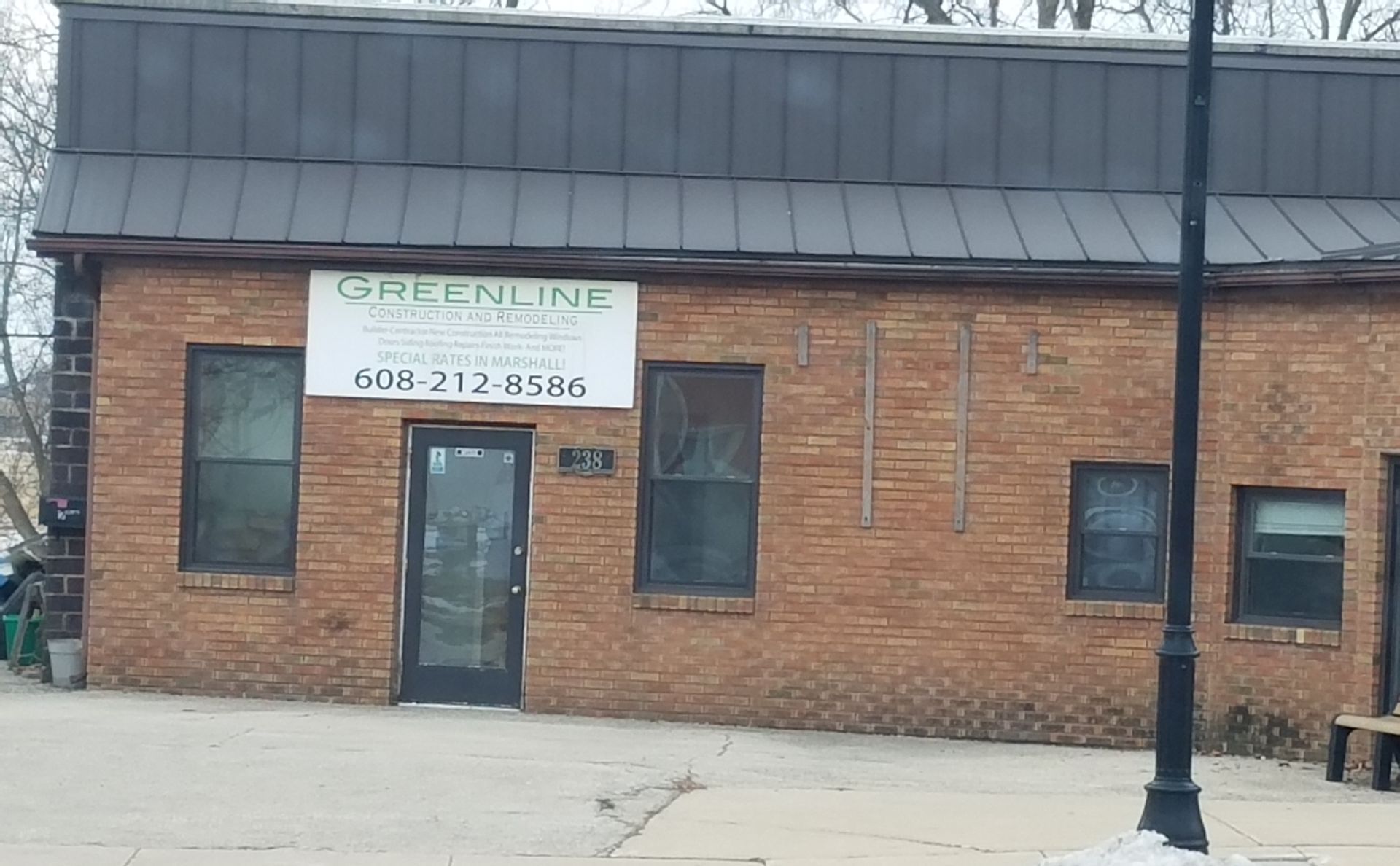 A one-story brick building with a dark metal roof, a centered entrance door, and a sign reading 