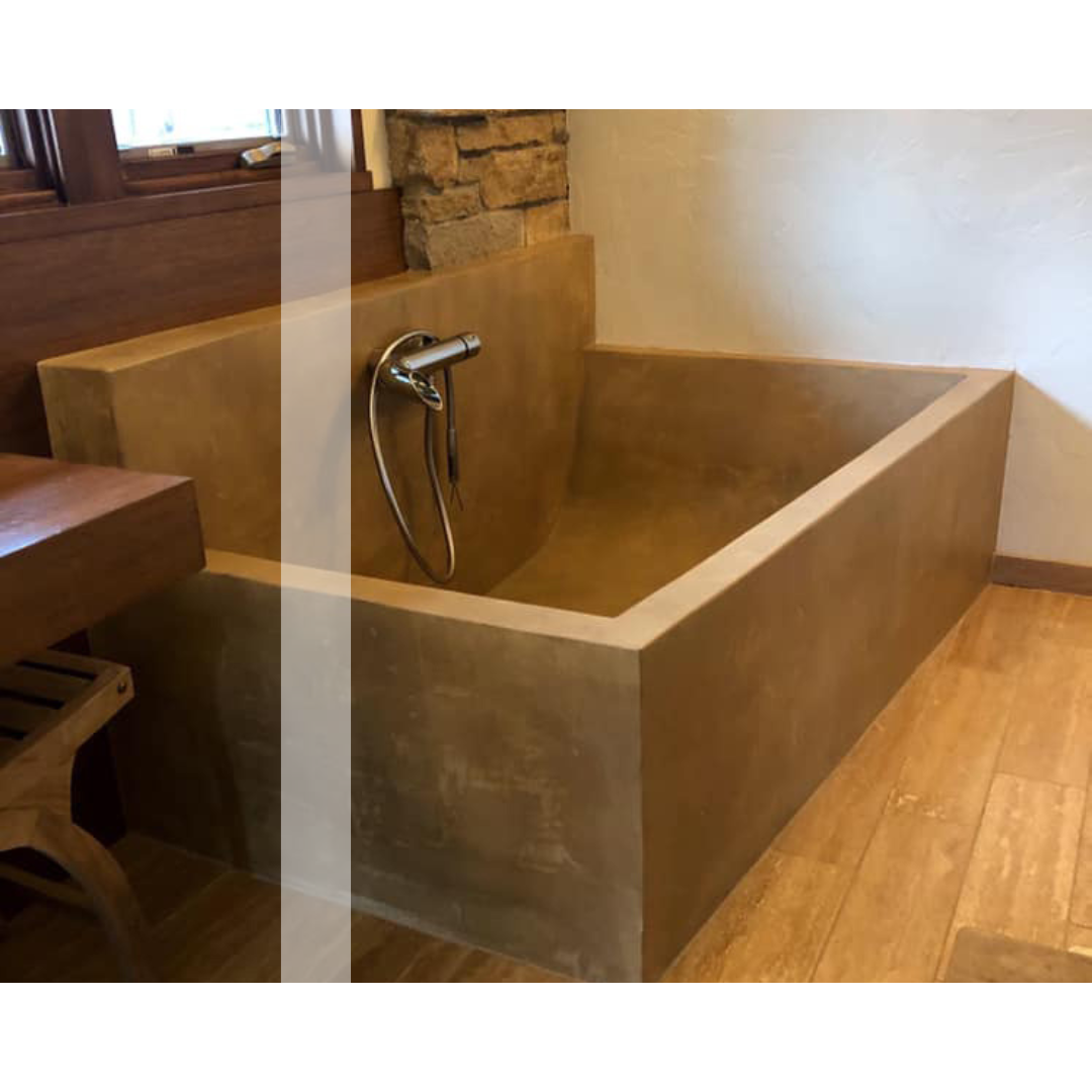 A concrete bathtub in a bathroom next to a window.
