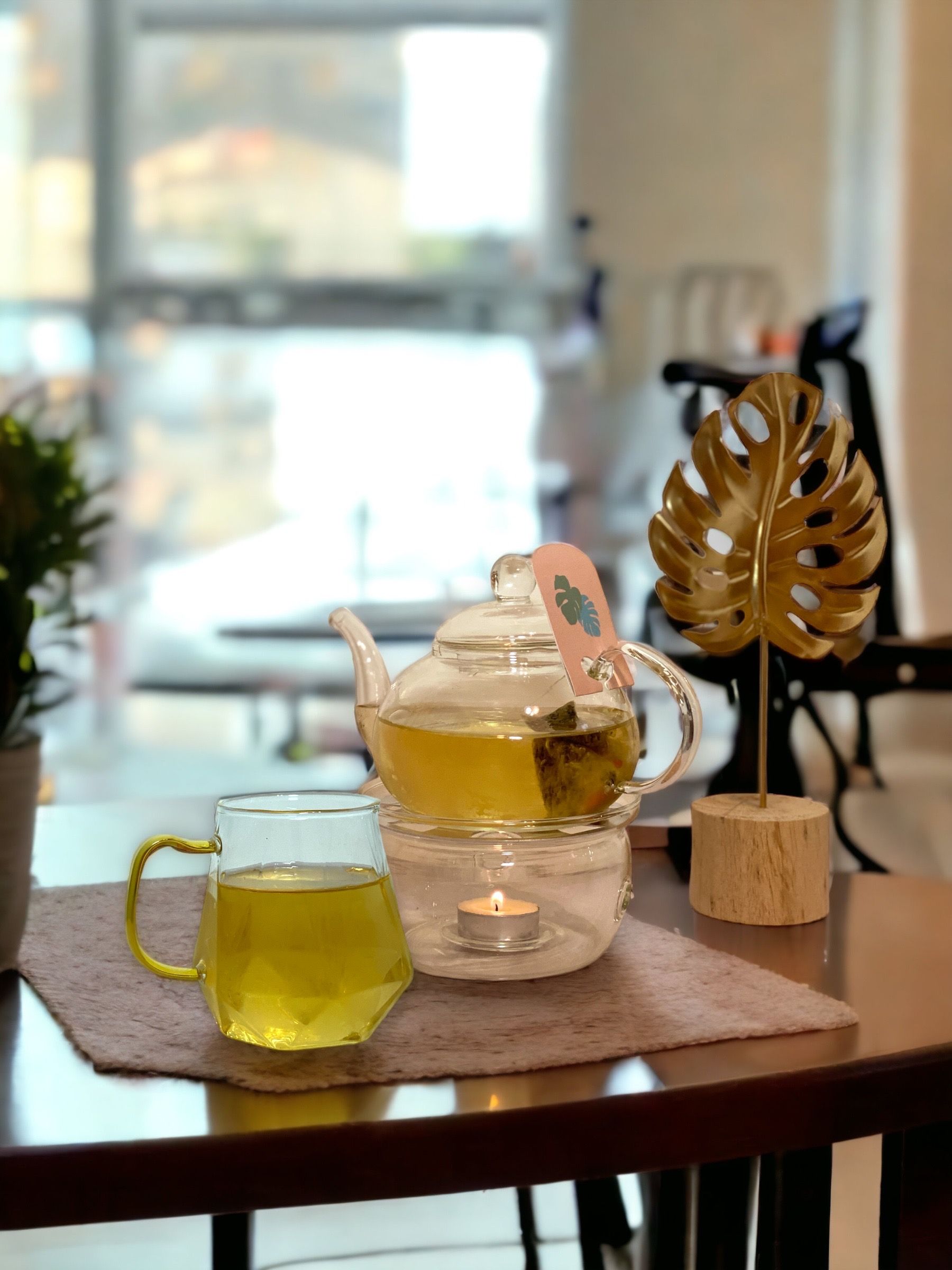木桌上放著玻璃茶壺和茶杯，旁邊放著一件金箔飾品。