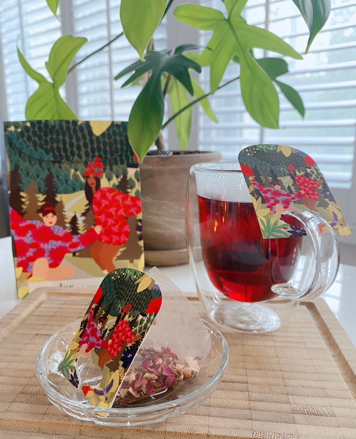 窗邊，一盆植物旁，托盤上擺放著色彩鮮豔的花卉卡片和一杯紅茶。