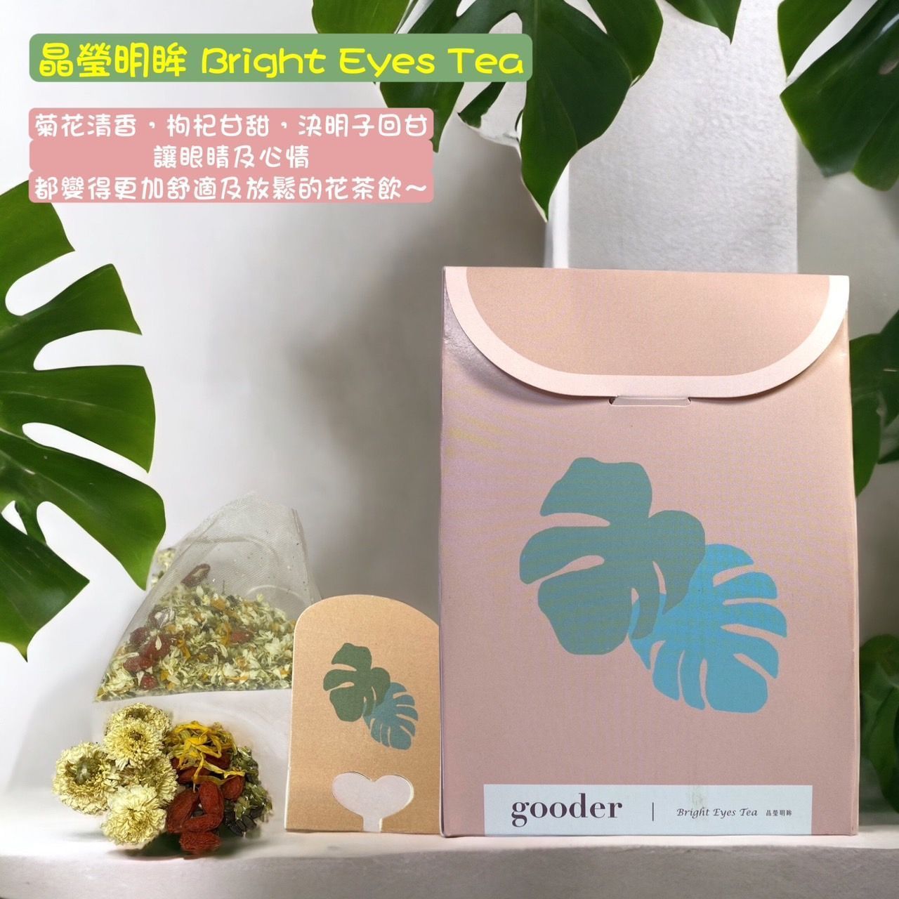 粉紅茶葉禮盒，印有藍綠色葉子標誌，內含茶包和鮮花，擺放在白色桌上，旁邊還有綠葉。