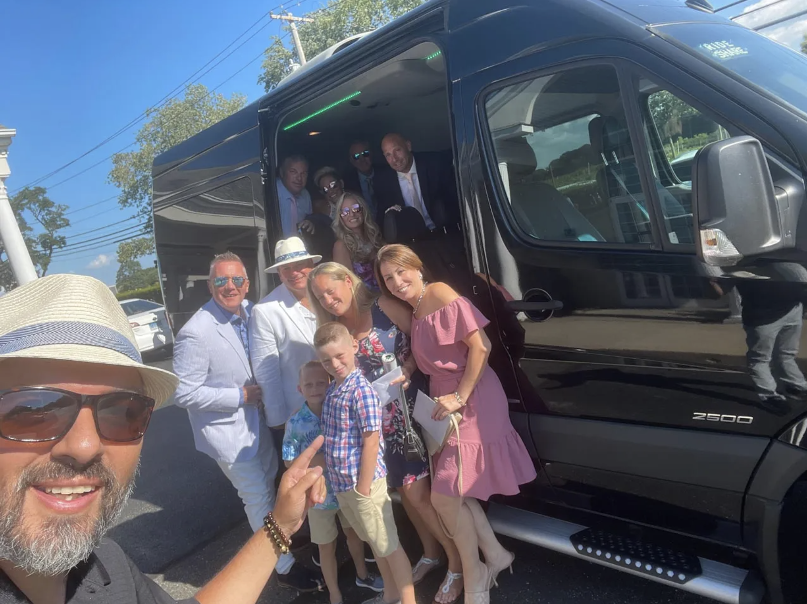 Group of people exiting a black van on a sunny day. Smiling, posing for photo.