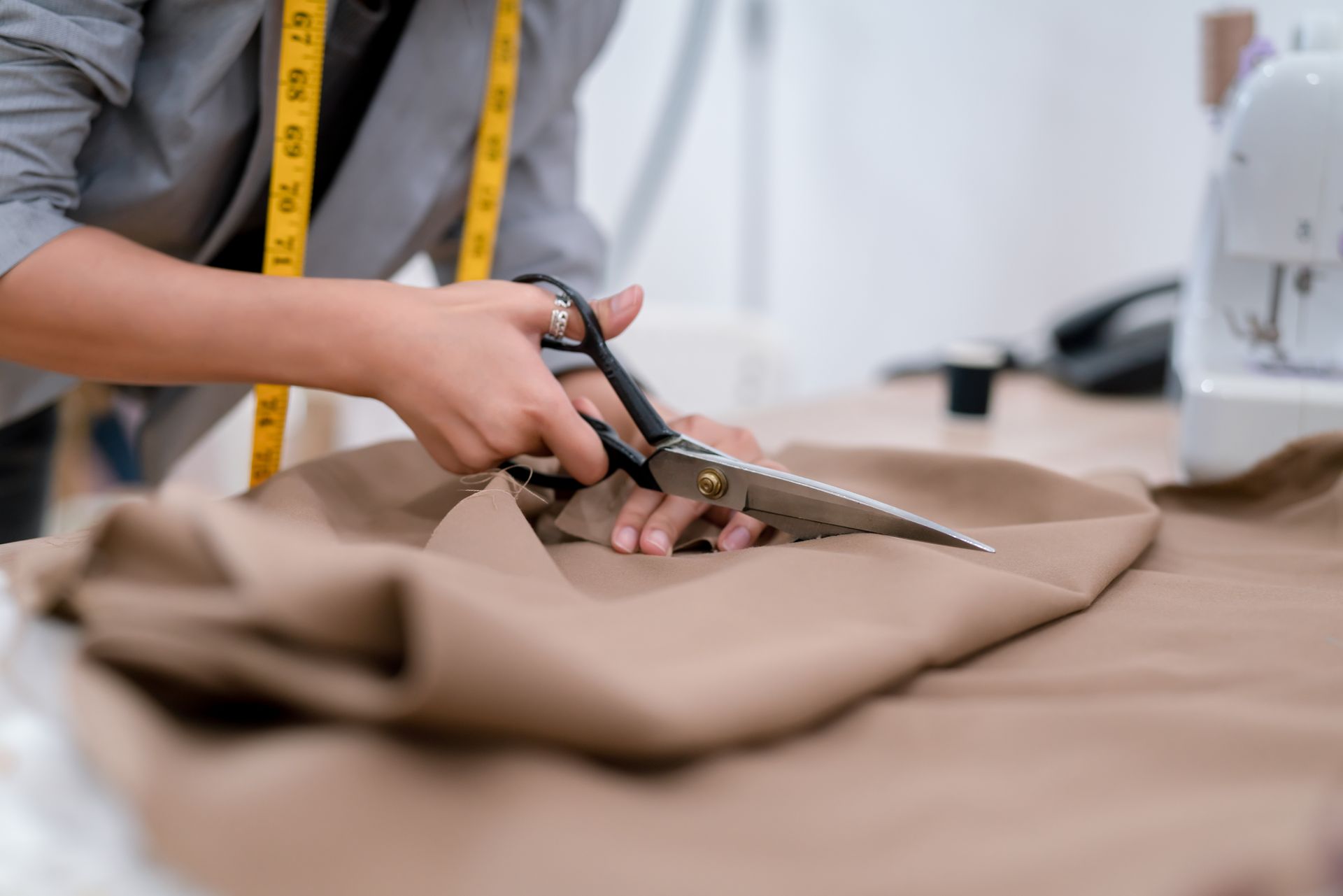 Person cutting tan fabric with large scissors in a sewing workspace