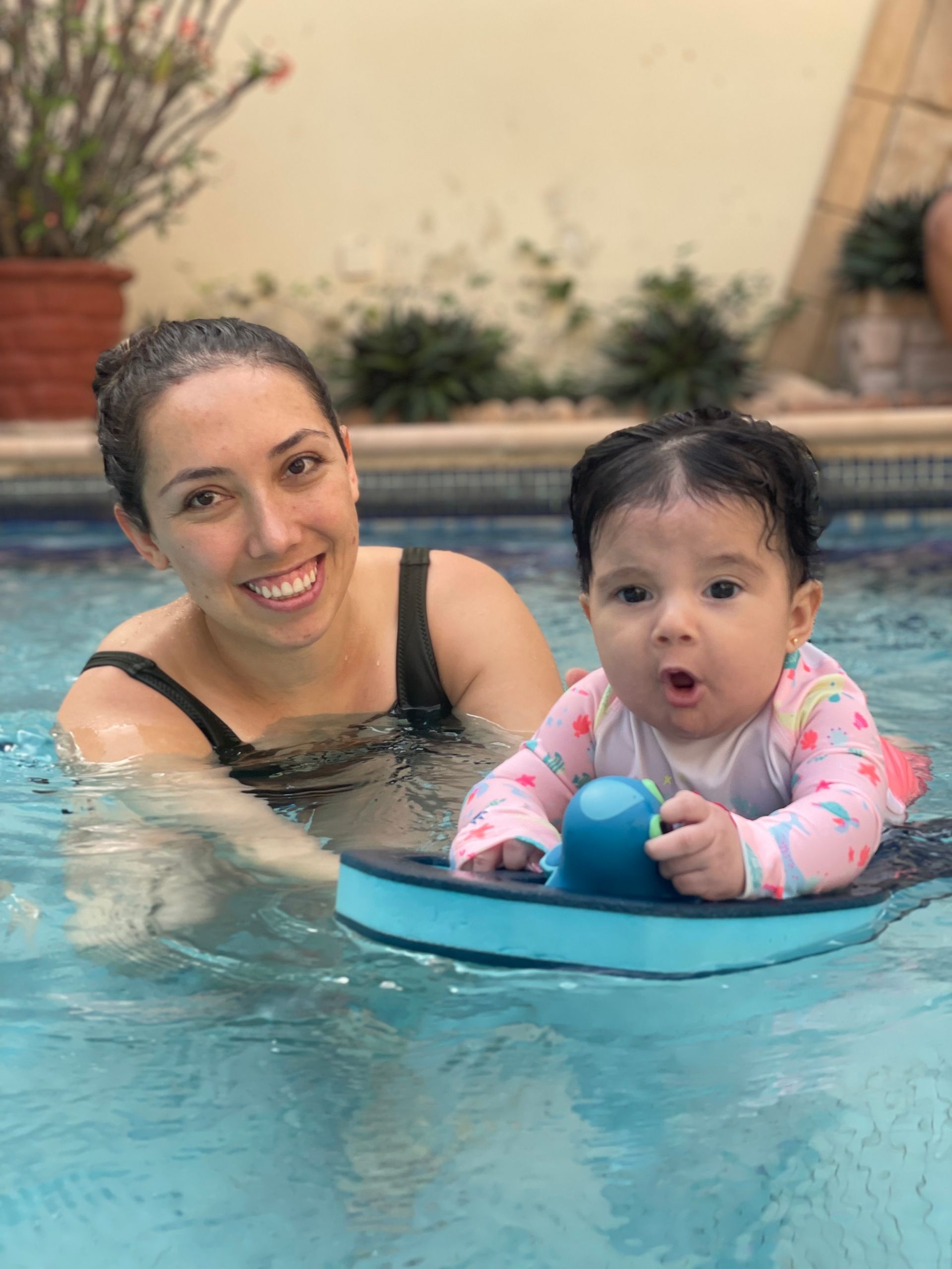 Woman and baby in a pool, smiling with the baby on a blue float.