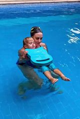 Woman holding a child in a blue swimming pool, both wearing blue flotation devices