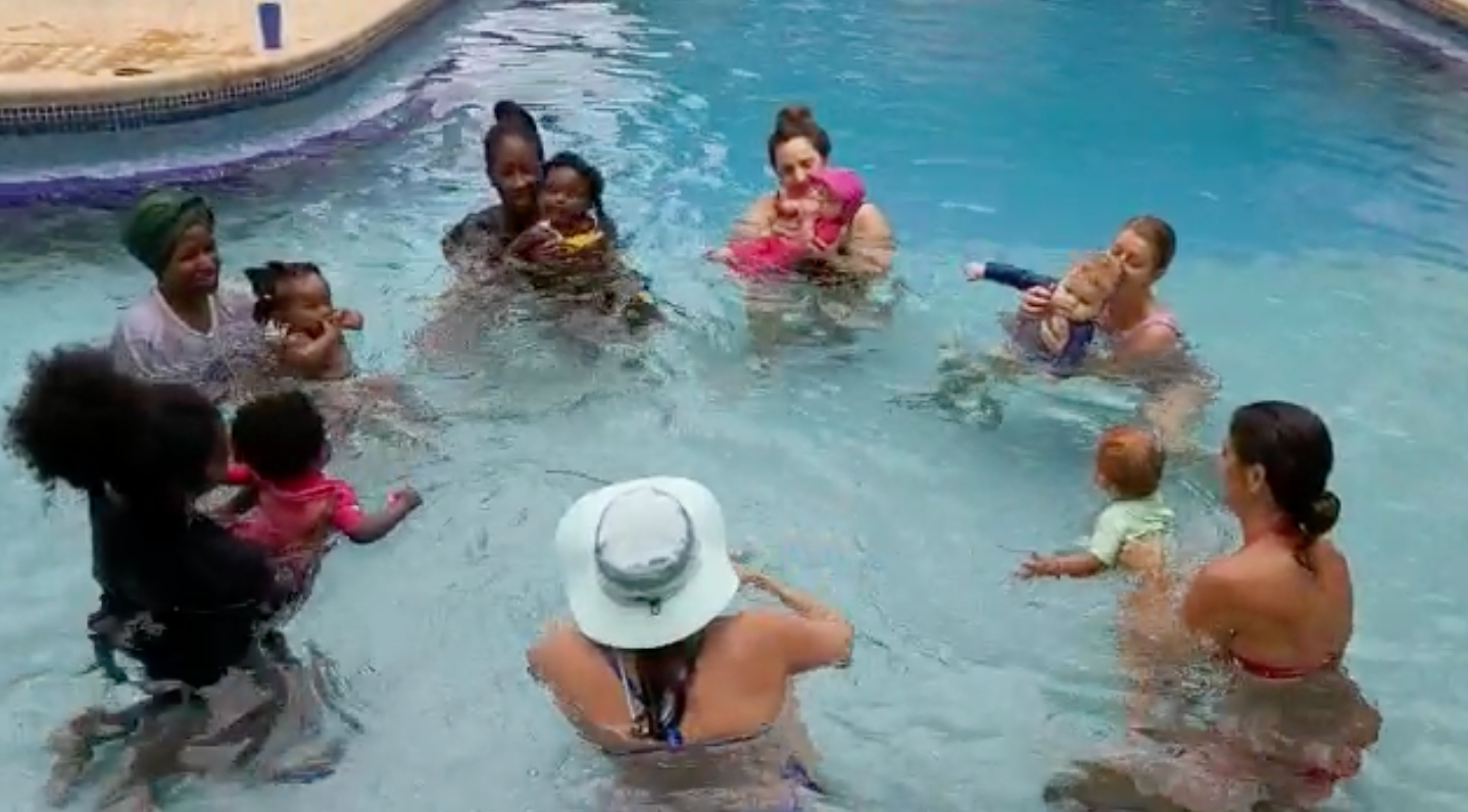 People in a swimming pool, splashing and chatting in a relaxed group circle.