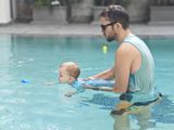 Adult holding a baby in a swimming pool, both wearing light blue swimwear.