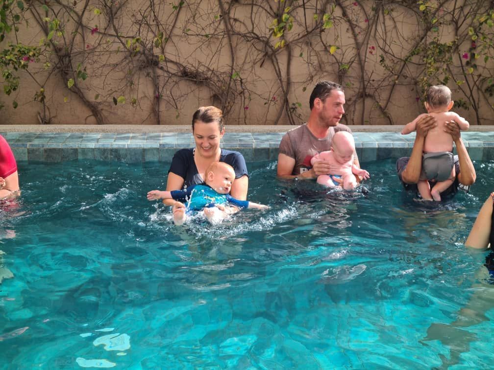 People relaxing in a turquoise pool near a stone wall and vines, splashing and holding drinks