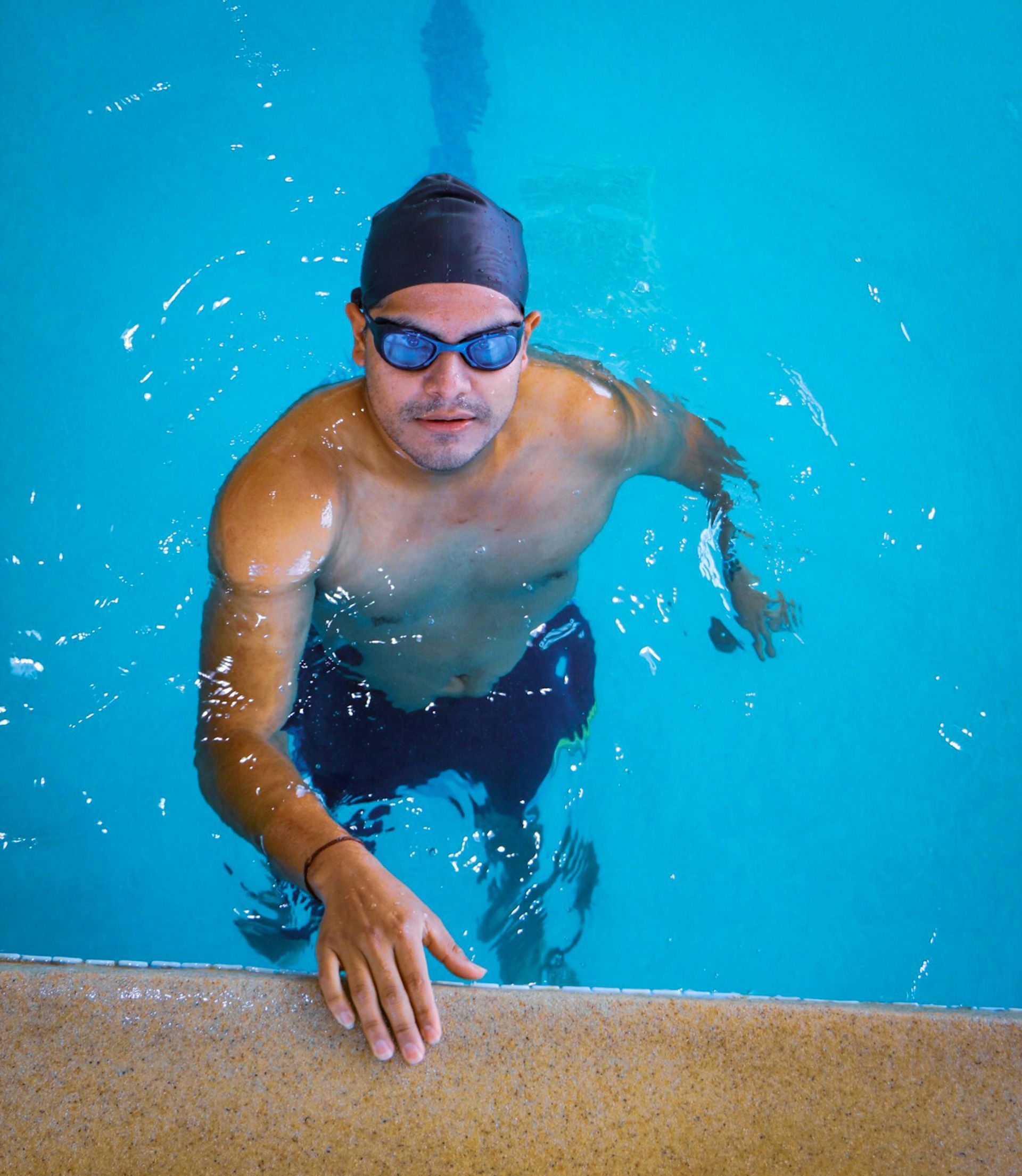 Swimmer in blue cap and goggles reaching up to the pool edge in bright turquoise water