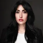 A woman with long black hair is wearing a white shirt and a black jacket.