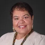 A woman wearing a white shirt and a necklace is smiling for the camera.