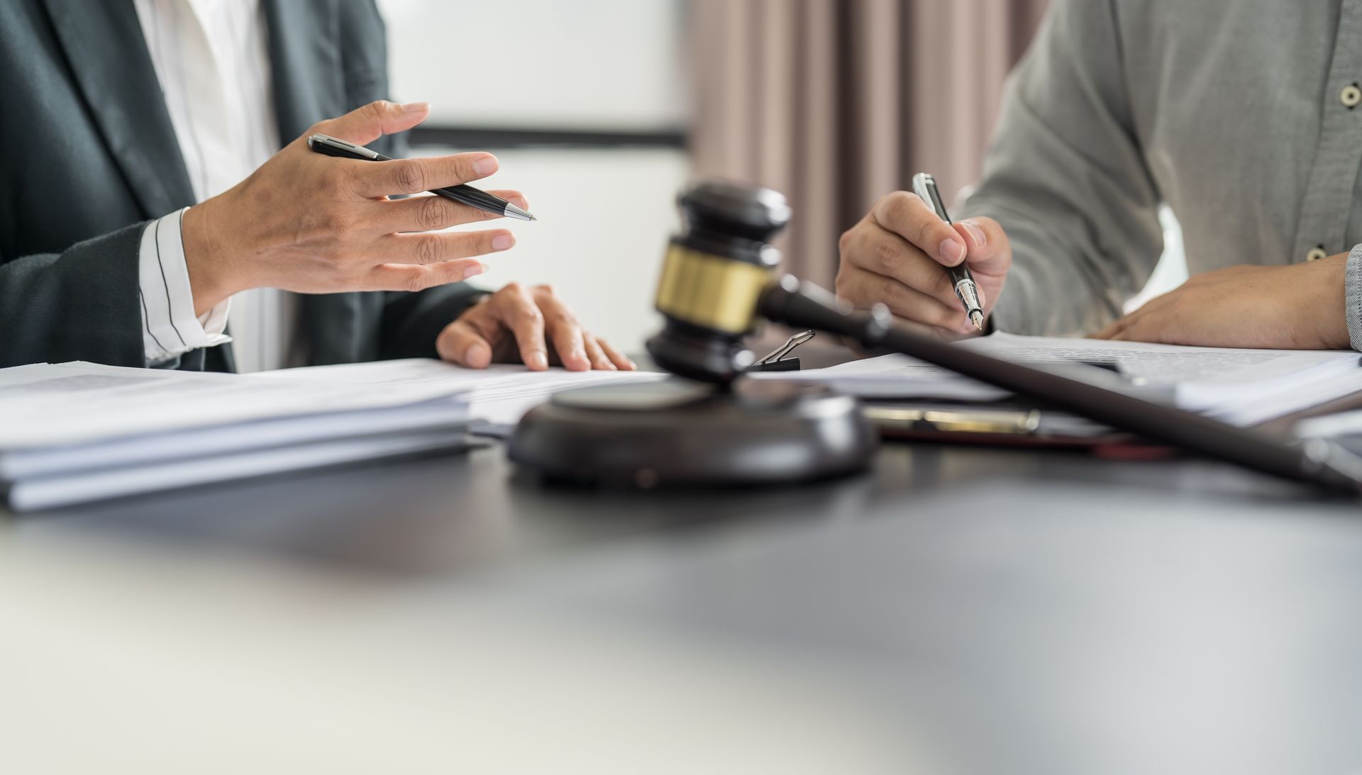 Gavel on table with people discussing paperwork, likely legal or business context.