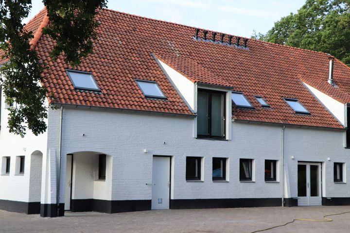 Wit huis met rood pannendak en dakkapellen, gezien vanaf de straat.