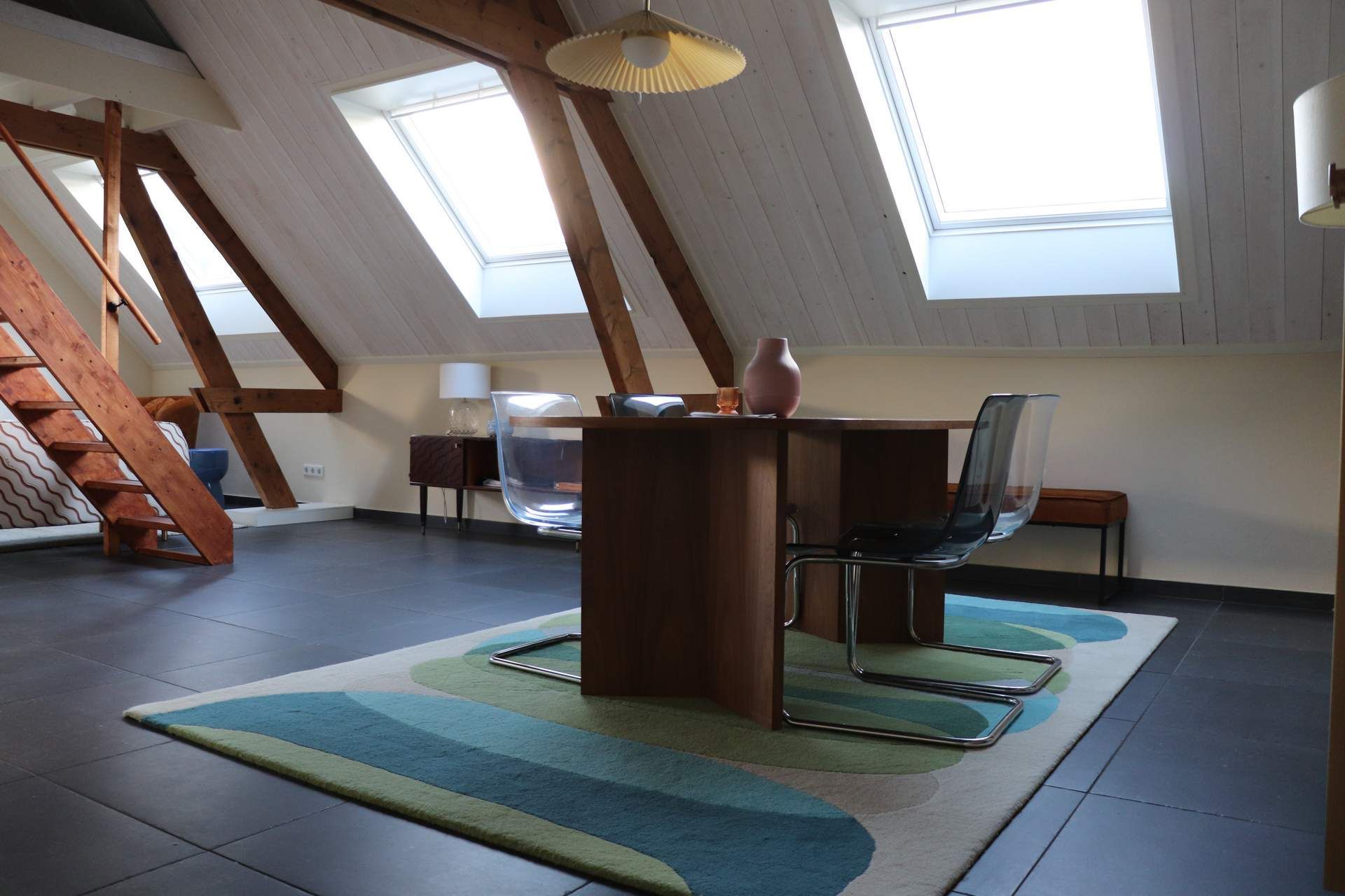 Attic office with slanted skylights, wooden table, chairs, and blue-green rug