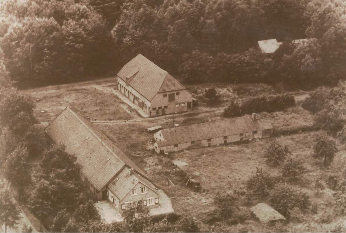 Sepia luchtfoto van landelijke schuren en boerderijgebouwen, omgeven door velden en bomen.