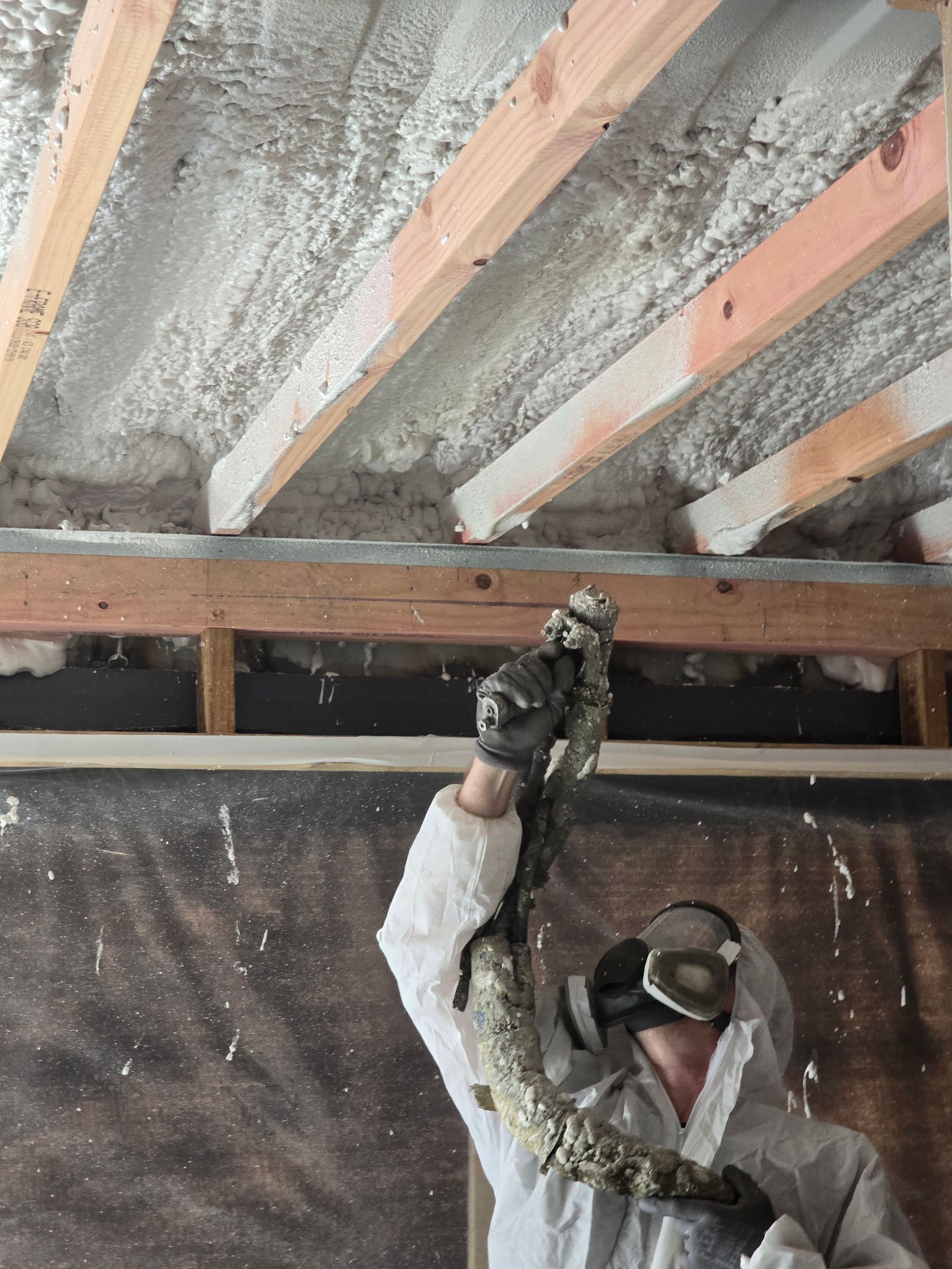 A man is spraying foam on the ceiling of a building.