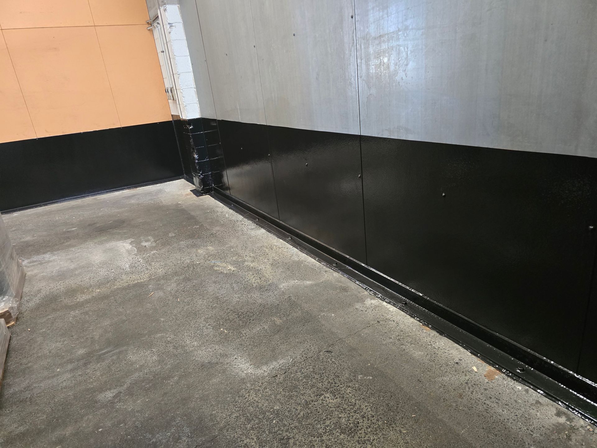 A corner of a room with a black wall and a concrete floor.