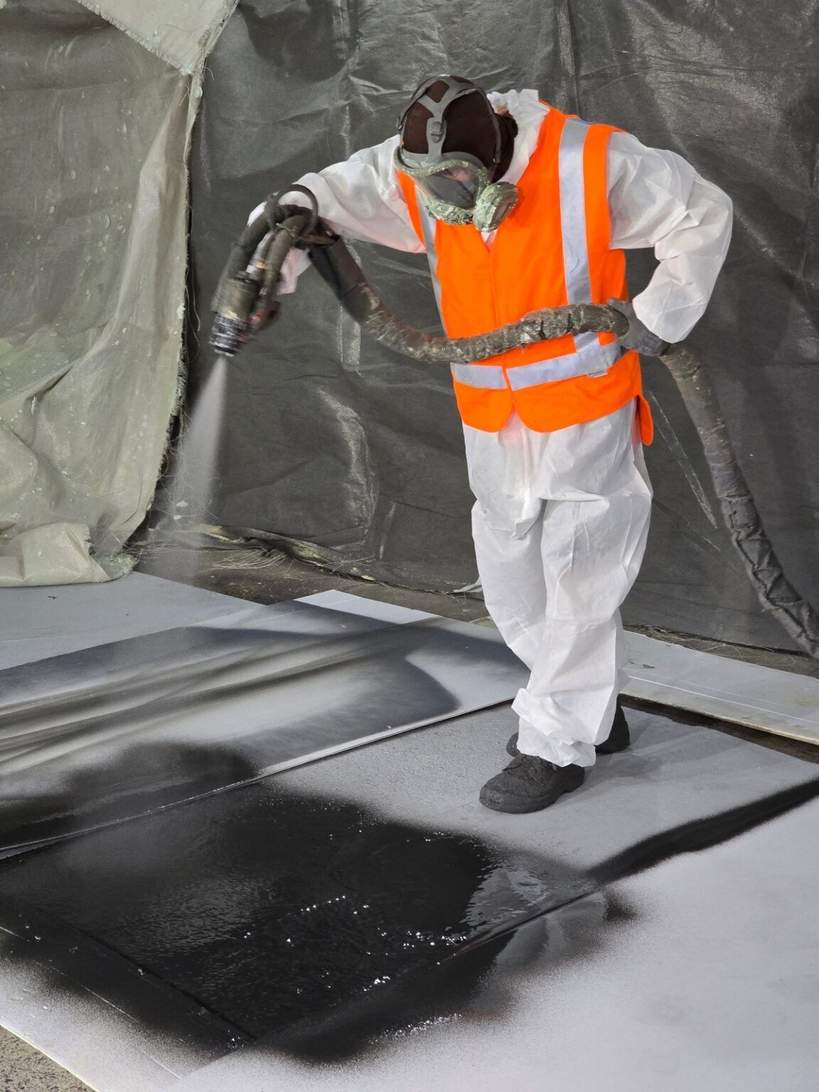 A man wearing an orange vest and safety vest is spraying something